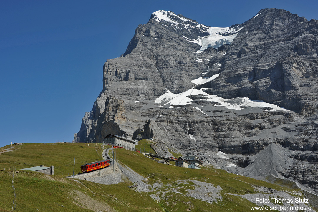Station Eigergletscher mit Eiger
Bei grossem Andrang werden die Züge mehrfach geführt. Der erste Zusatzzug in Form eines BDhe 2/4 befindet sich unmittelbar vor dem Tunnelportal,
ein zweiter folgt ihm in kurzem Abstand. Der mit 2 Doppeltriebwagen BDhe 4/8 geführte Stammzug befindet sich noch in der Station Eigergletscher.
