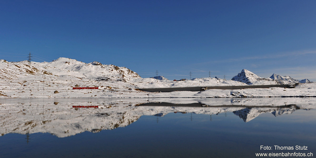 Spiegelungen im Lej Nair
Während der kleinere Lej Pitschen bereits weitgehend zugefroren ist, hat es im Lej Nair erst wenig Eis.
Dafür sind die Spiegelungen im ruhigen Wasser umso beeindruckender. Rechts ist die Staumauer des Lago Bianco zu sehen.
