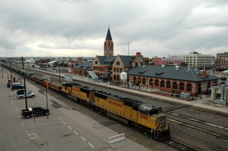 Union Pacific Schotterzug, als Zuglok SD70M #4266. Im Hintergrund das "Depot" (= Bahnhof) von Cheyenne, WY, heute ein Museum und Sitz der chamber of commerce.
