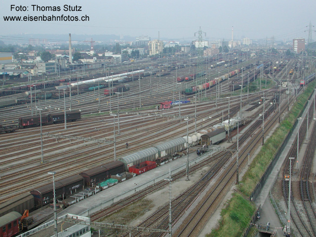 B-Gruppe
In der oberen Bildhälfte ist die B-Gruppe (Formationsgleise Nord - Süd), ganz rechts oben wieder das Stellwerk West. Am rechten Bildrand sind noch 2 Gleise der F-Gruppe zu erkennen. Der DPZ (unterhalb des Stellwerks West) kommt von Basel SBB und bringt die Besucher in den Rangierbahnhof. Er befährt die "Umfahrung Mitte", die normalerweise von Transitzügen und Lokfahrten benutzt wird.
